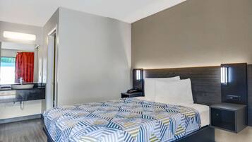 A hotel room with a large bed, a bedside table with a lamp, a modern bathroom with a sink and mirror, and a red curtain.