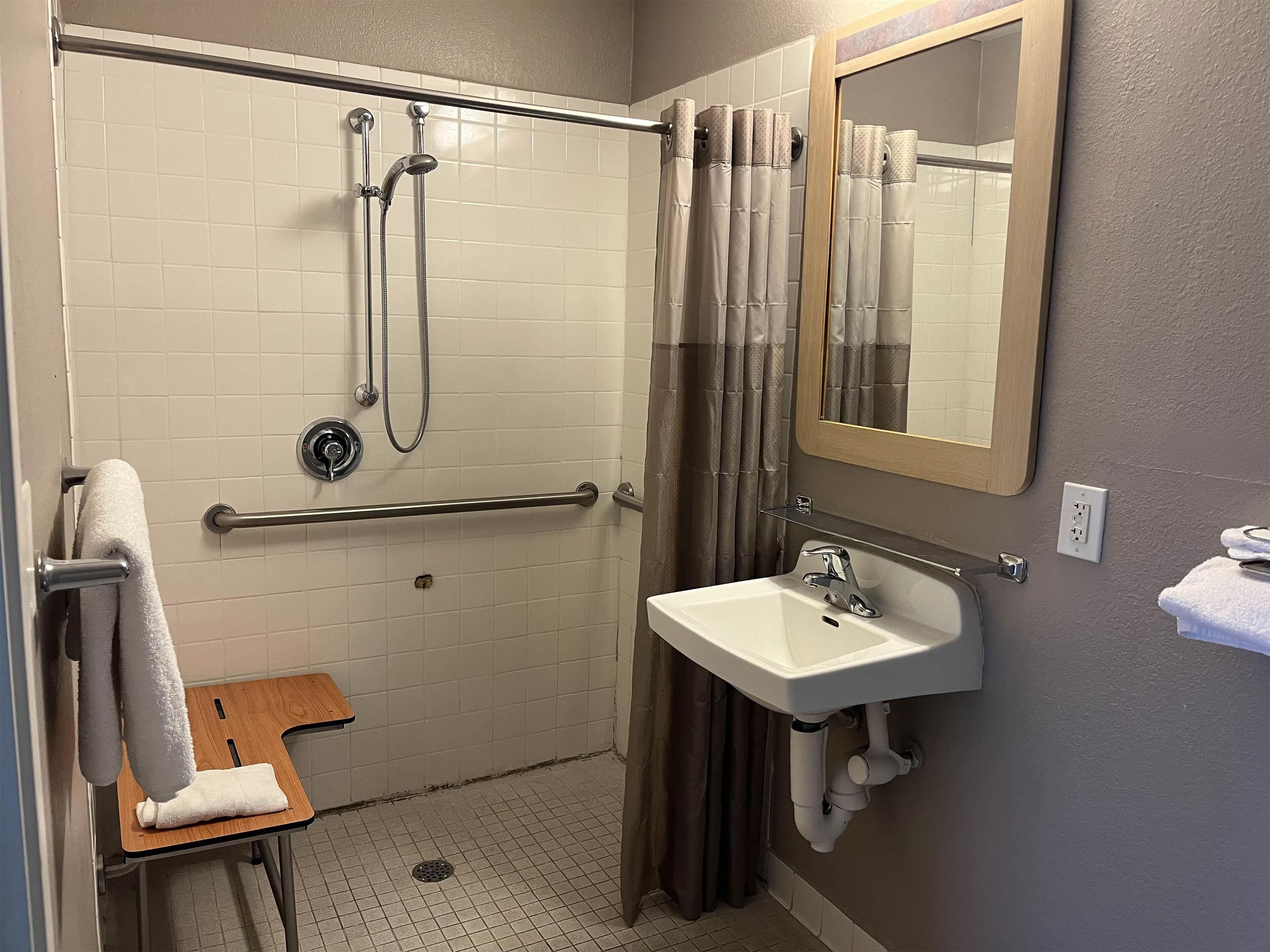 A bathroom with a shower, a sink, a mirror, and a towel rack.