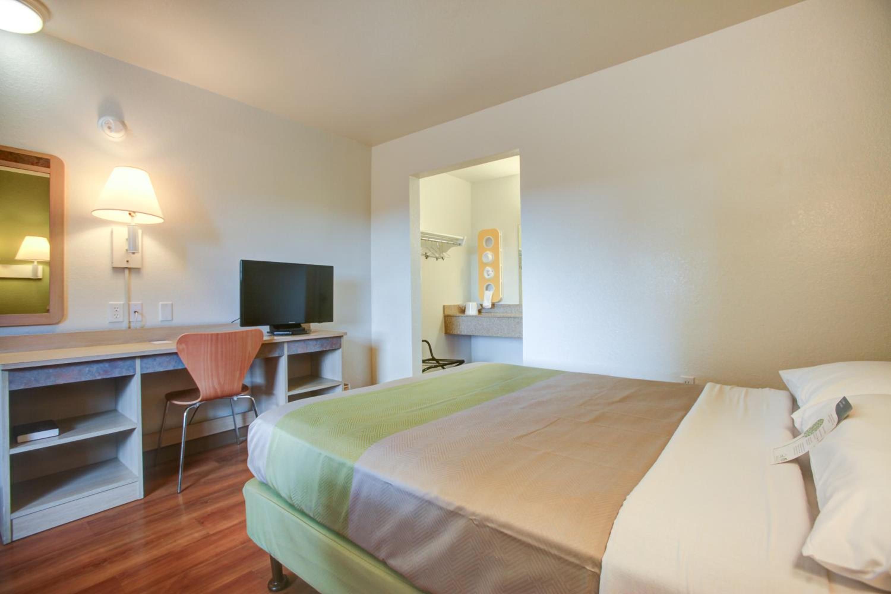A hotel room with a bed, a desk with a chair, a television, and a mirror.