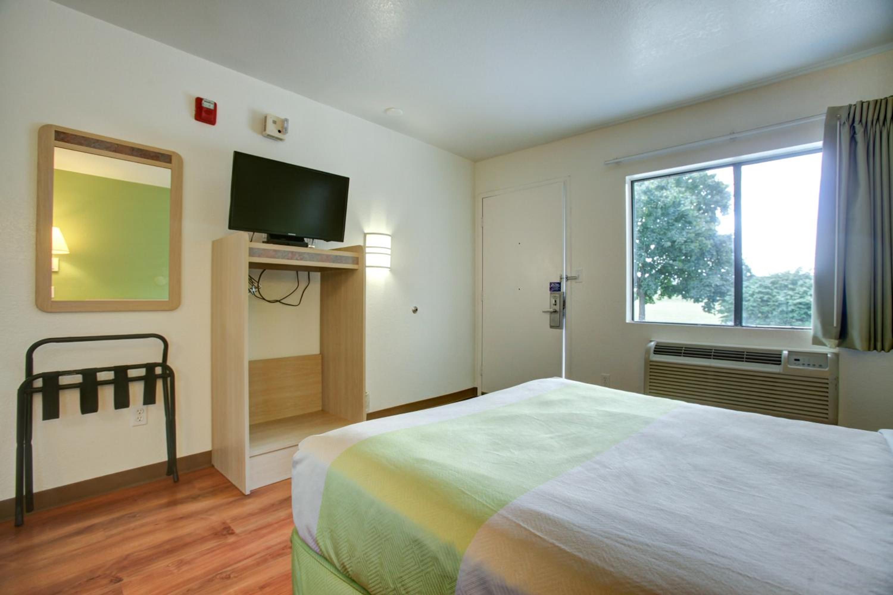 A hotel room with a bed, a television, a desk, a chair, a window, and a door.