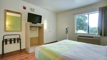 A hotel room with a bed, a television, a desk, a chair, a window, and a door.