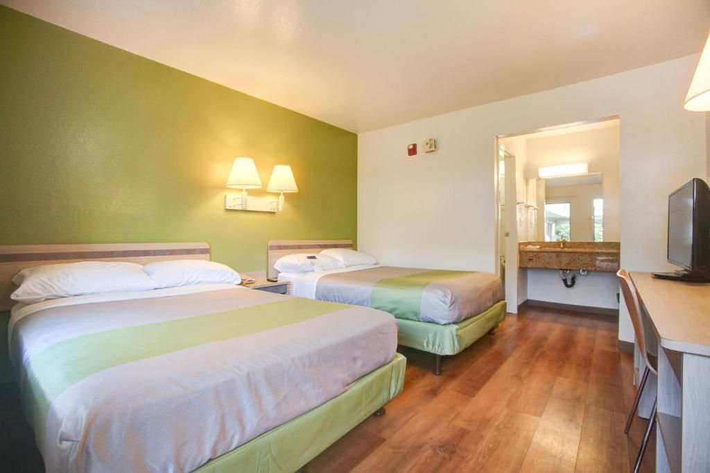 A hotel room with two beds, a desk, a television, and a bathroom visible through an open door.