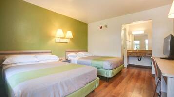 A hotel room with two beds, a desk, a television, and a bathroom visible through an open door.