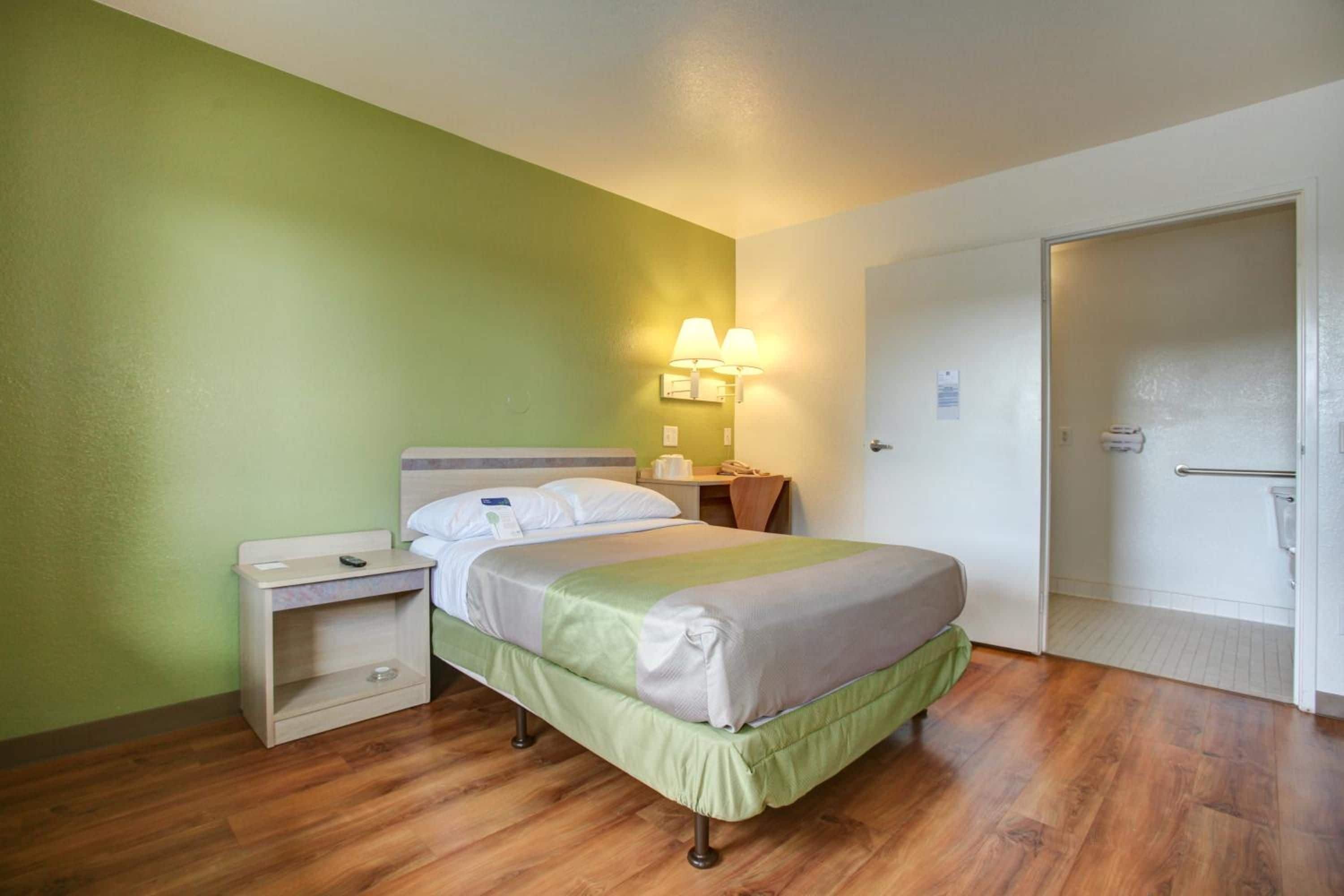 A hotel room with a bed, bedside table, lamp, and a door.