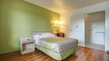A hotel room with a bed, bedside table, lamp, and a door.