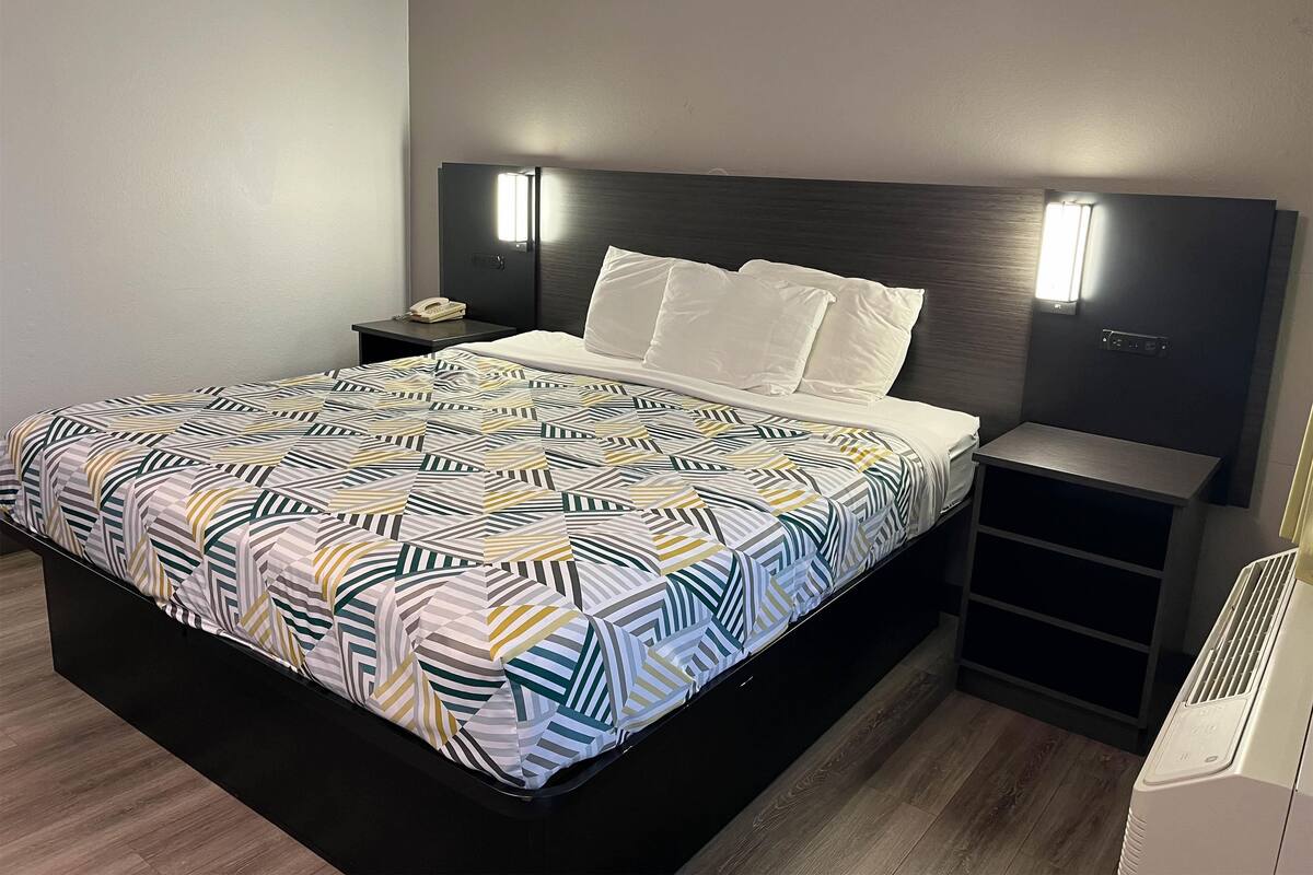 Ein modernes Hotelzimmer mit einem großen Bett, einem Nachttisch mit Lampe und einer fest installierten Heizung.