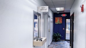 A hallway with a night window sign, a painting on the wall, and a potted plant.