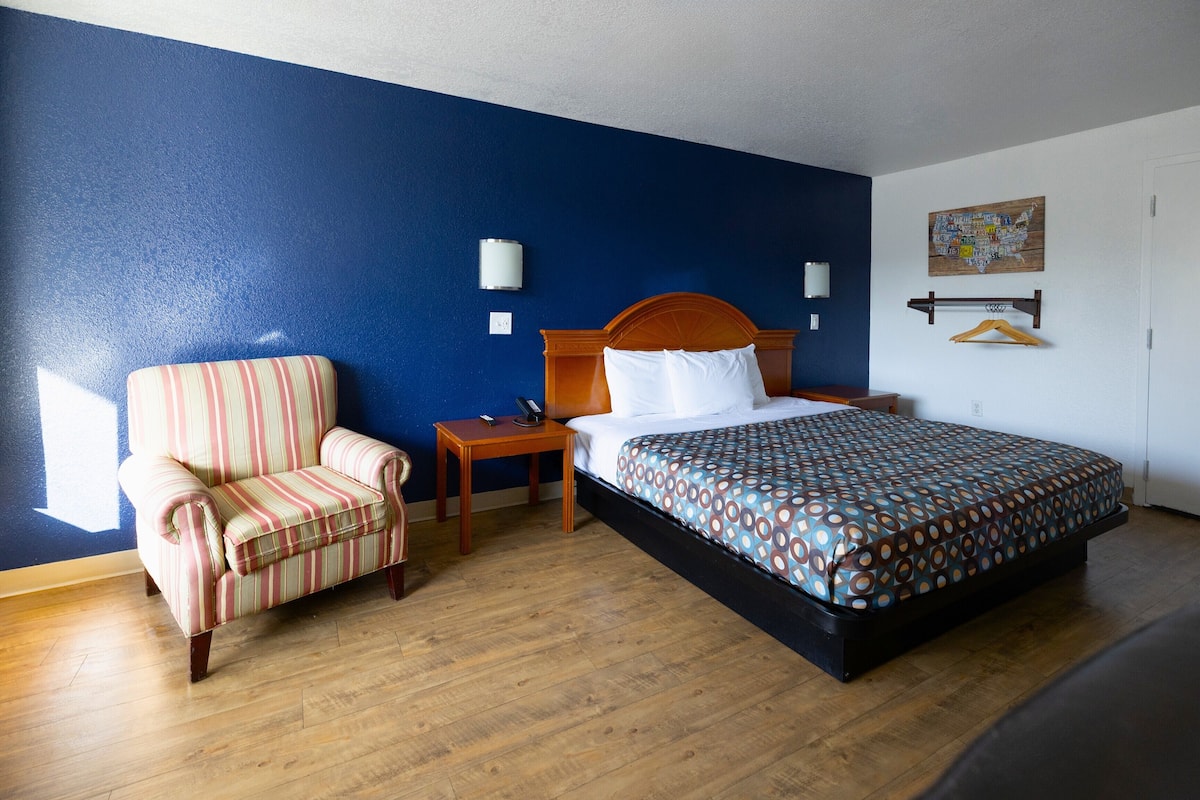 Une chambre d'hôtel avec un lit, un fauteuil à rayures, une table de chevet et un porte-manteau fixé au mur.