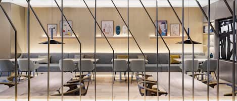 Un interior moderno con suelo de madera, sofás grises y una zona de comedor central con mesas y sillas.