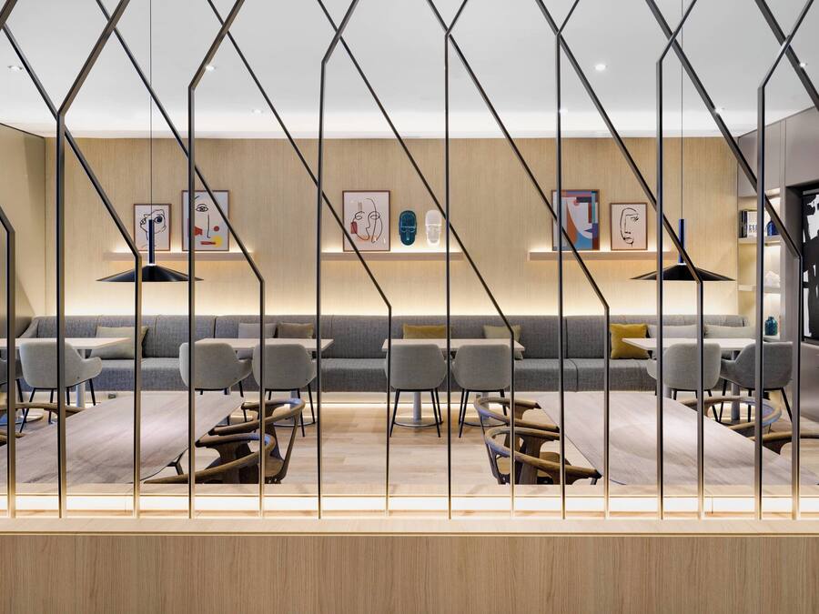 Un interior moderno con suelo de madera, sofás grises y una zona de comedor central con mesas y sillas.