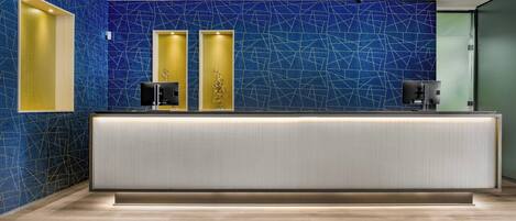 A reception area with a modern design, featuring a blue mosaic wall, a reception desk, and a glass door leading to the hallway.