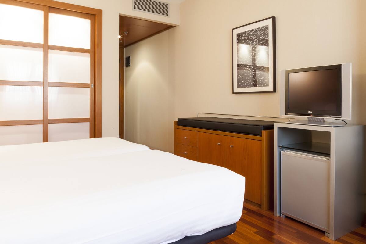 Ein Hotelzimmer mit einem Bett, einem kleinen Kühlschrank, einem Fernseher und einem Holzkasten.