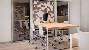 A modern meeting room with a large table, white chairs with wheels, and a large screen.