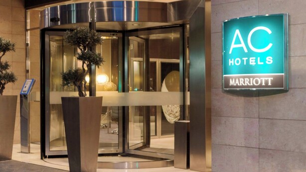 Entrada de un hotel con puerta de cristal, un letrero que dice "TARRAGONA" y otro letrero que indica "AC HOTELS MARRIOTT".
