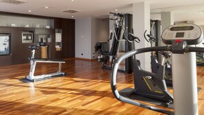 Un gimnasio con equipo de ejercicio, suelo de madera y pared espejada.