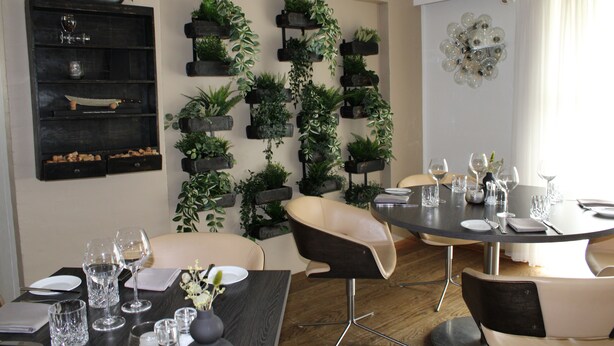 A dining area with a round table set for four, surrounded by modern chairs. A wall-mounted plant display adds greenery to the space. - Hotel Hedemarken (Grindsted)