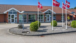 A building with a red-tiled roof and a glass entrance. There are four flags in front of the building. - Hotel Hedemarken (Grindsted)