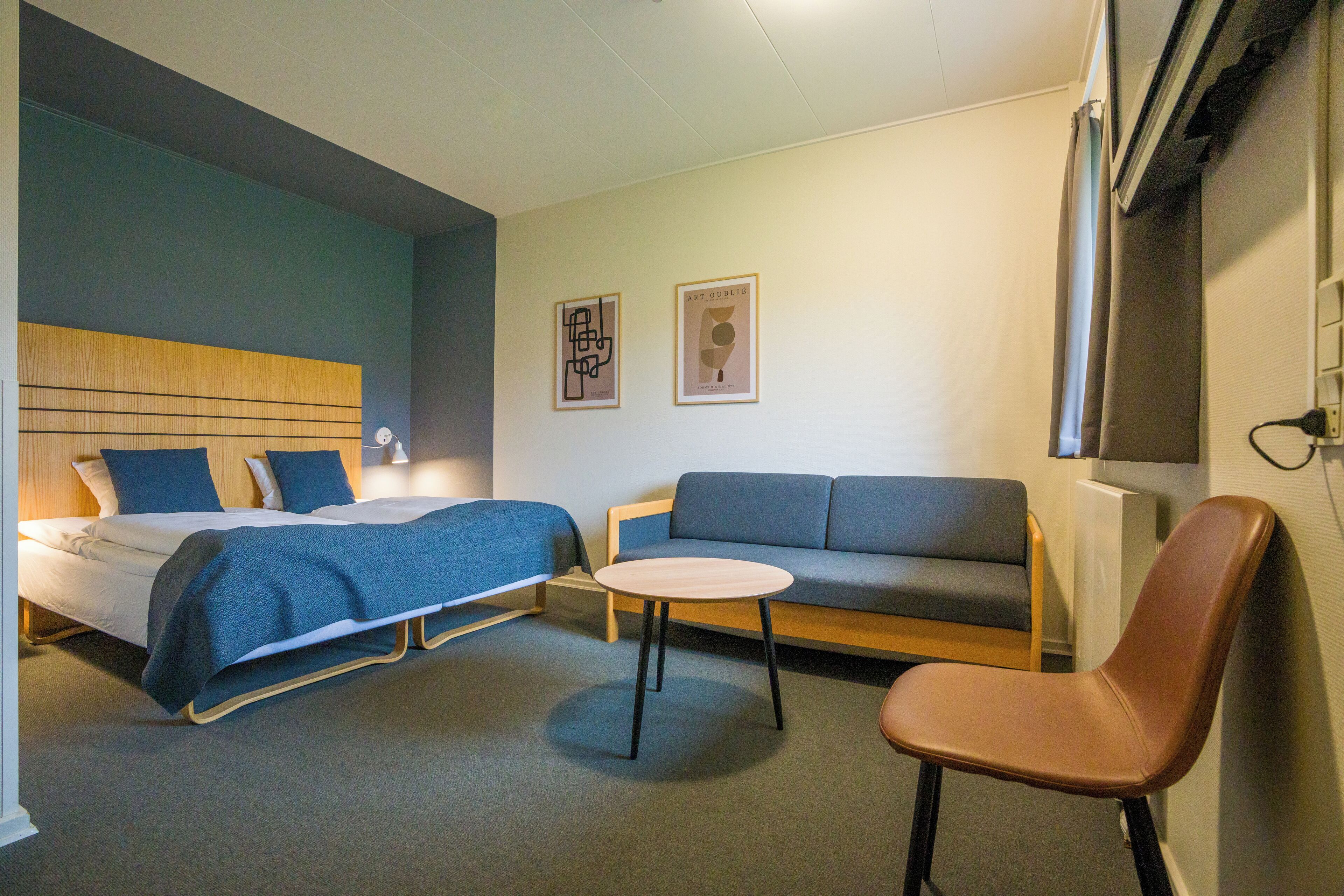 A modern hotel room with a bed, a sofa, a small table, and a chair.