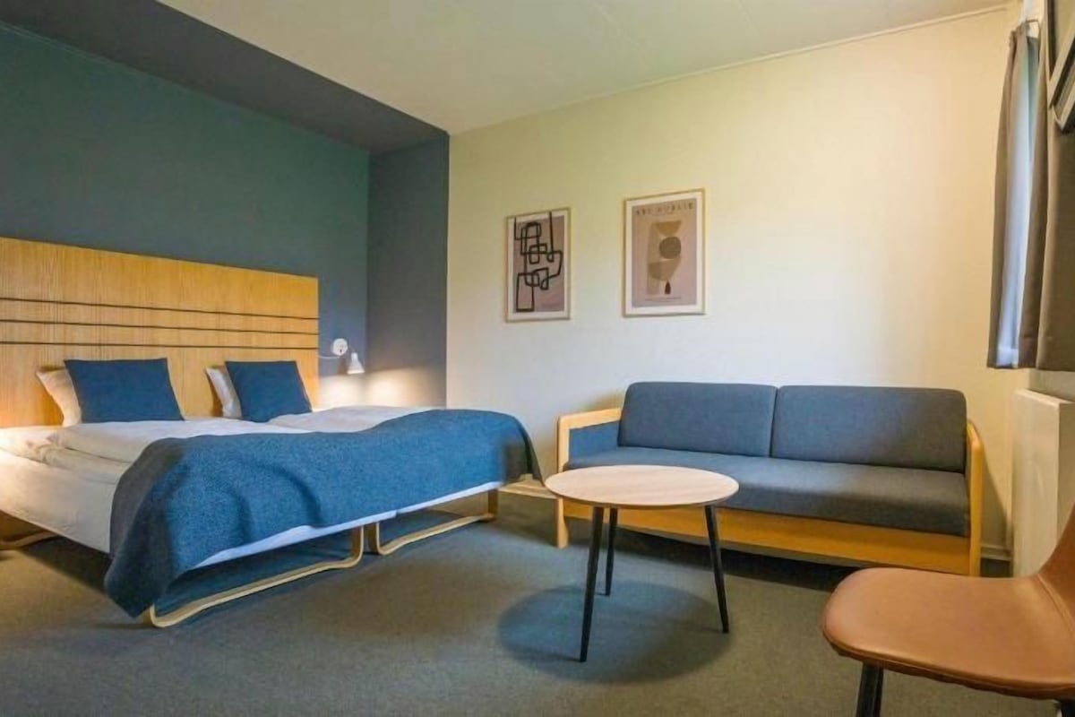 A hotel room with a bed, a sofa, a chair, and a small table.