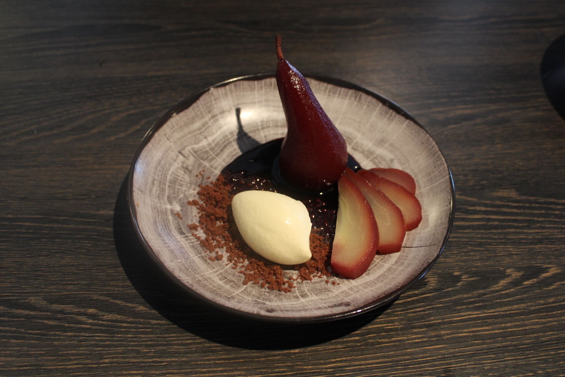 A dessert plate with a pear, apple slices, and a scoop of ice cream on a textured ceramic plate.