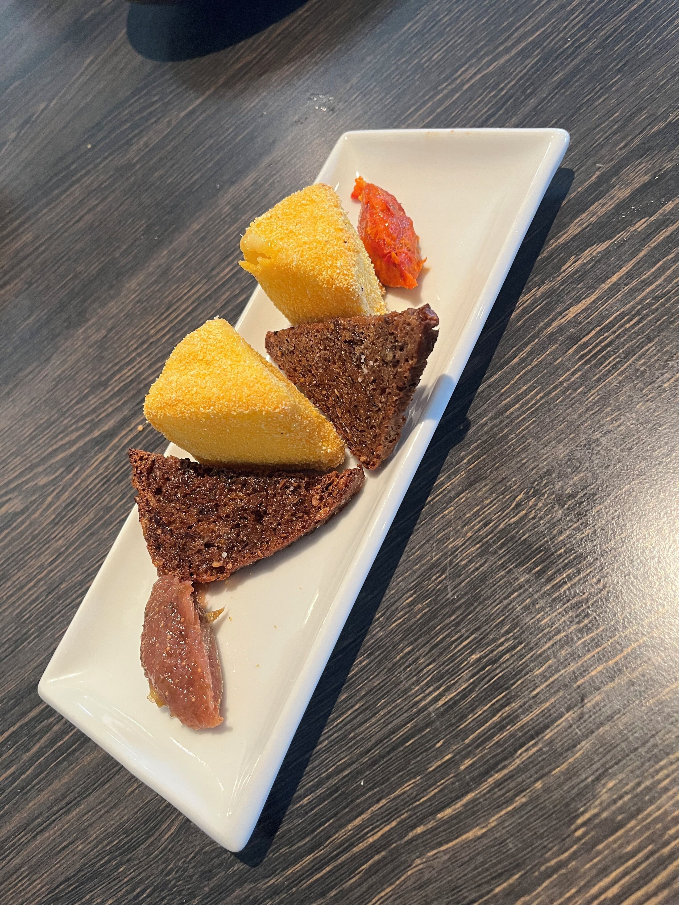 A white rectangular plate with three pieces of food on a dark wooden table.