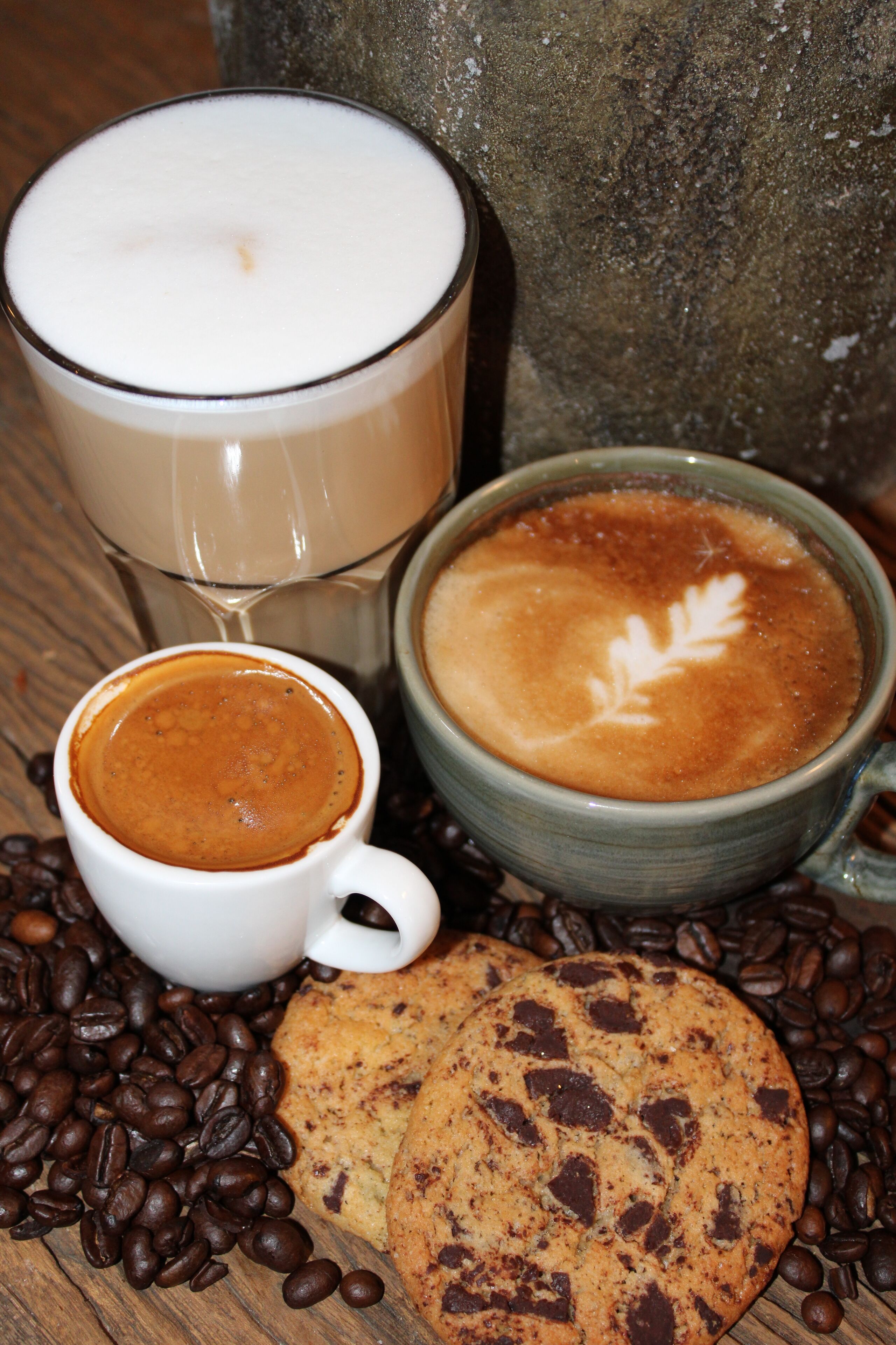 A cup of coffee, a glass of milk, and a cookie surrounded by coffee beans.