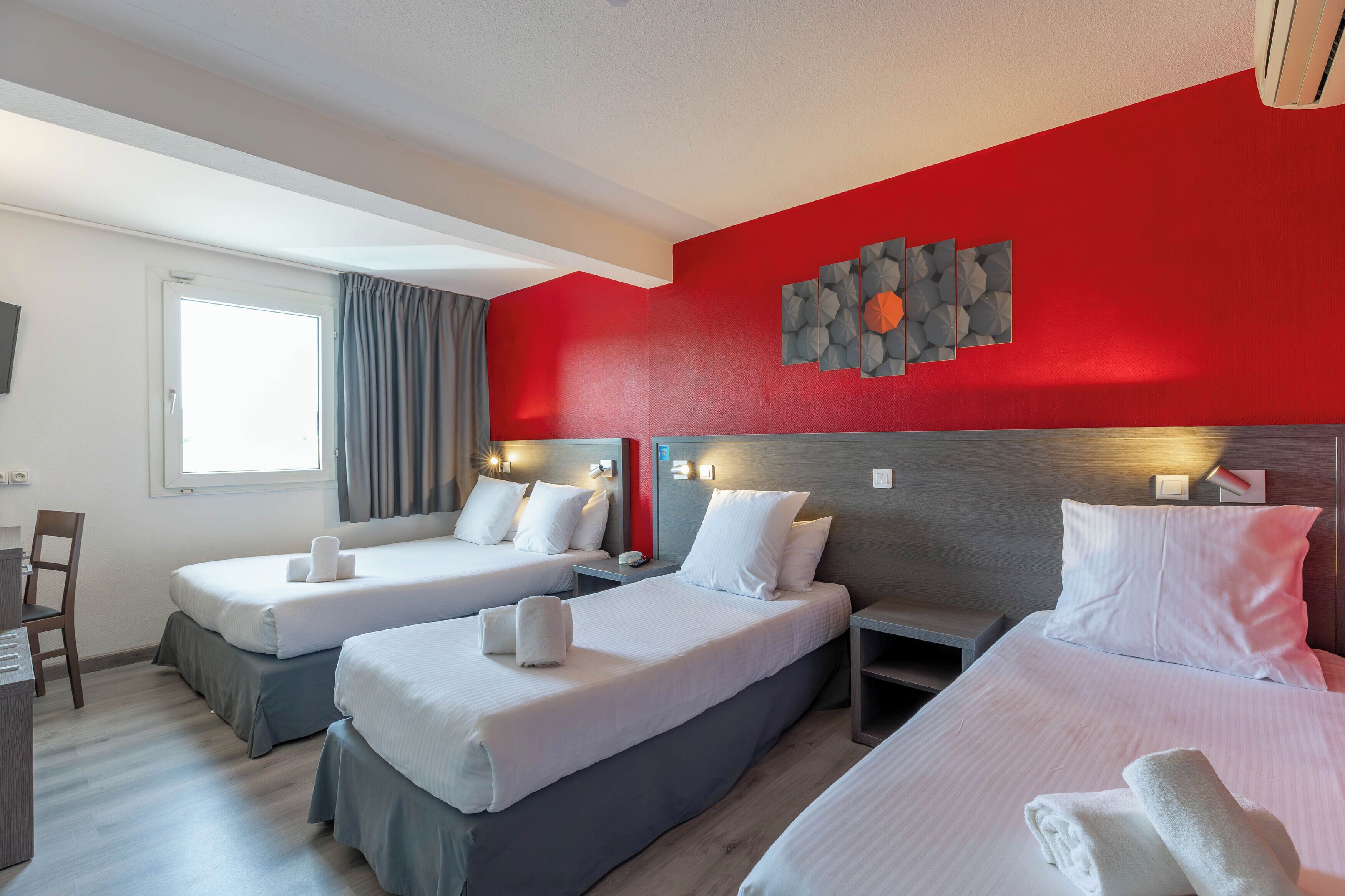 Habitación de hotel con dos camas, un escritorio y una ventana con cortinas.