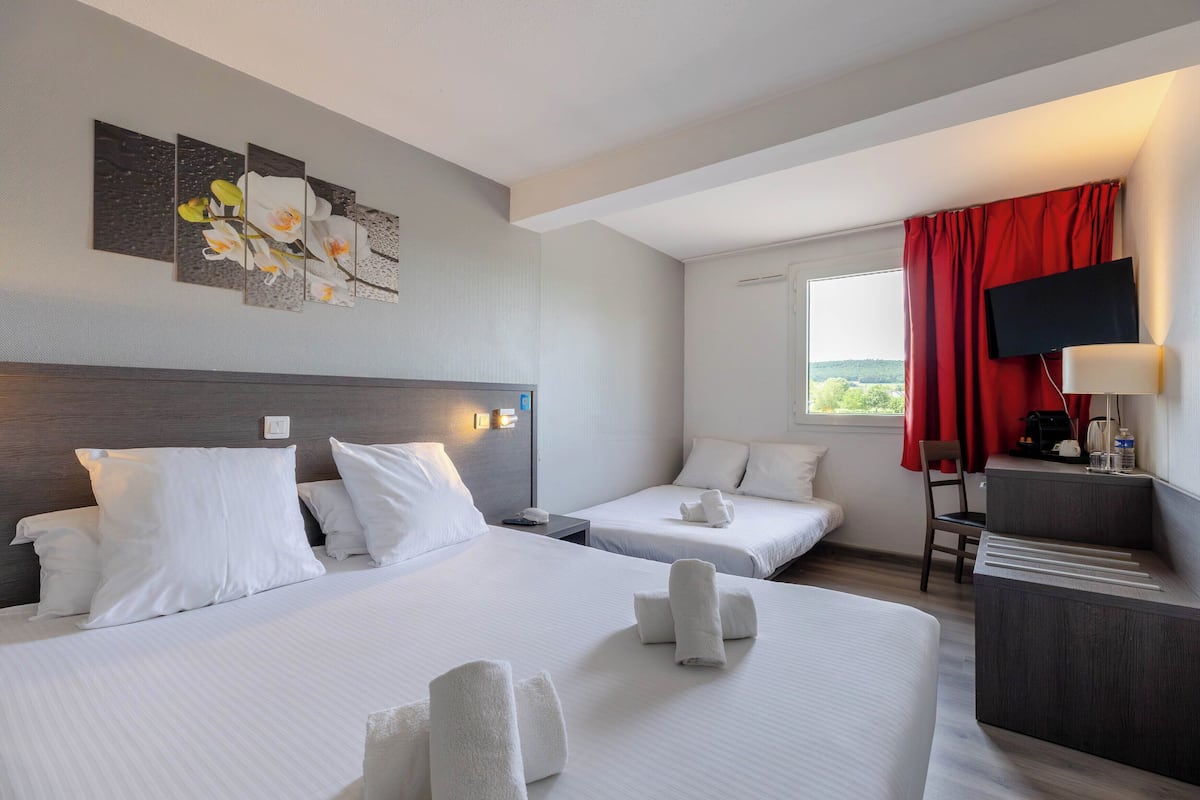 Habitación de hotel con dos camas, un escritorio, un televisor y una ventana con cortina roja.