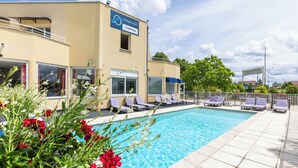 A swimming pool with lounge chairs, a building with a sign, and greenery. - The Originals City, Hôtel Restaurant L'Ormichal Dijon Sud. (Marsannay-la-Cote)