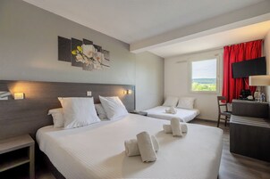 Habitación de hotel con dos camas, un escritorio, un televisor y obras de arte en la pared.