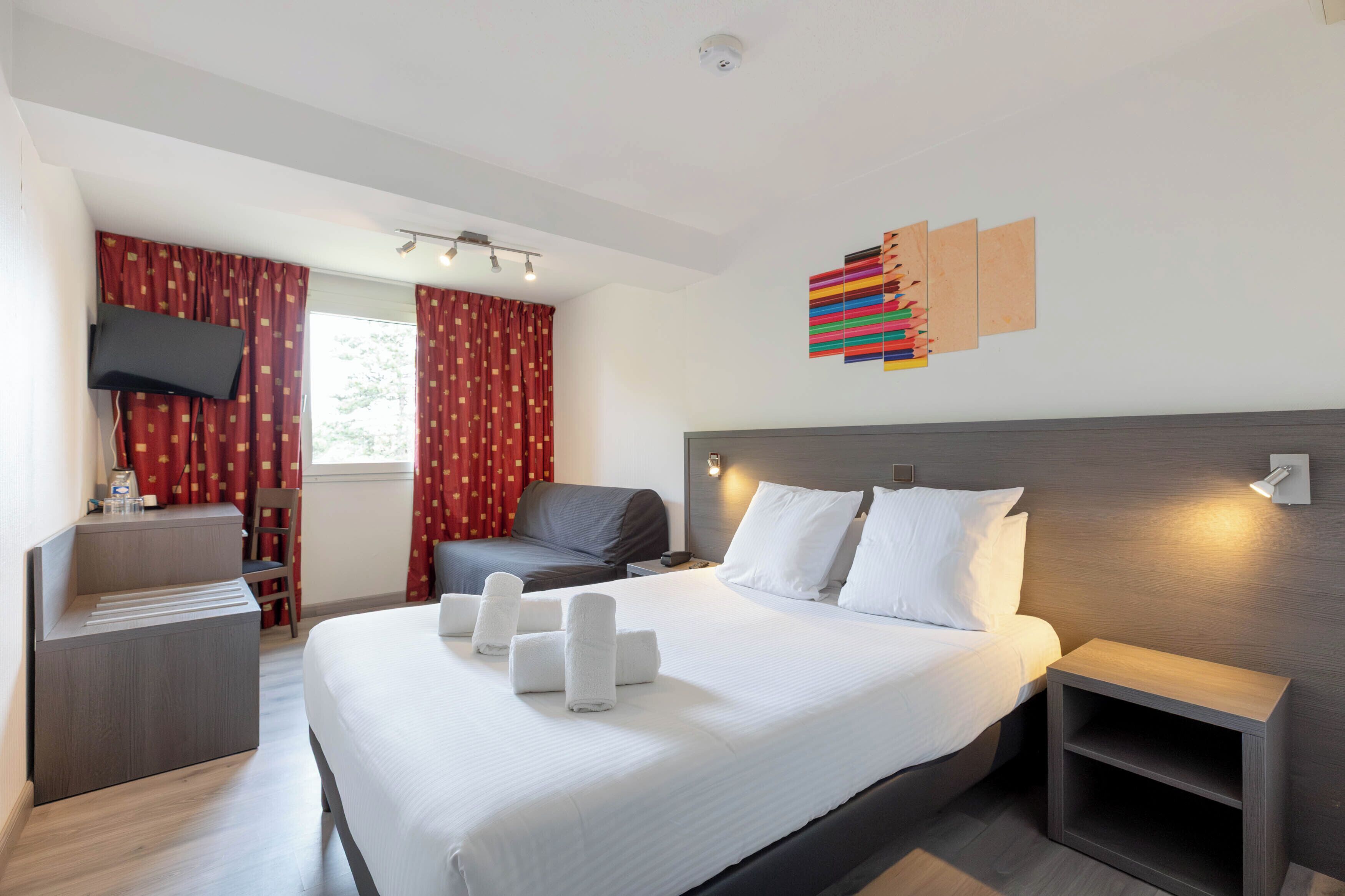 A modern hotel room with a large bed, a desk, a chair, and a TV.