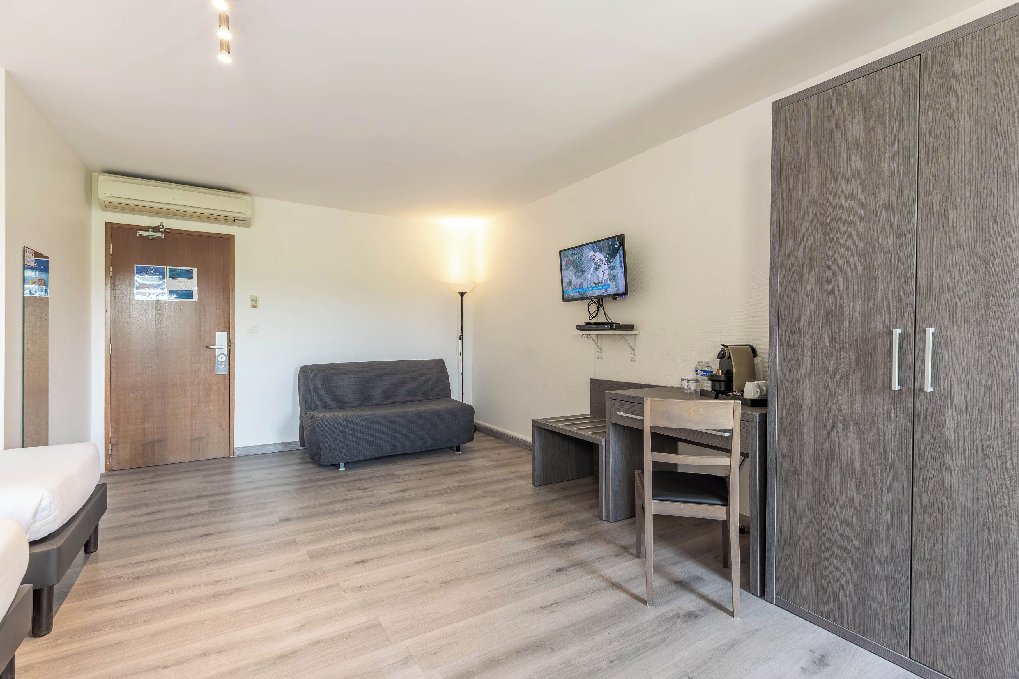 Una habitación de hotel con cama, sofá, escritorio con silla, televisor y armario.