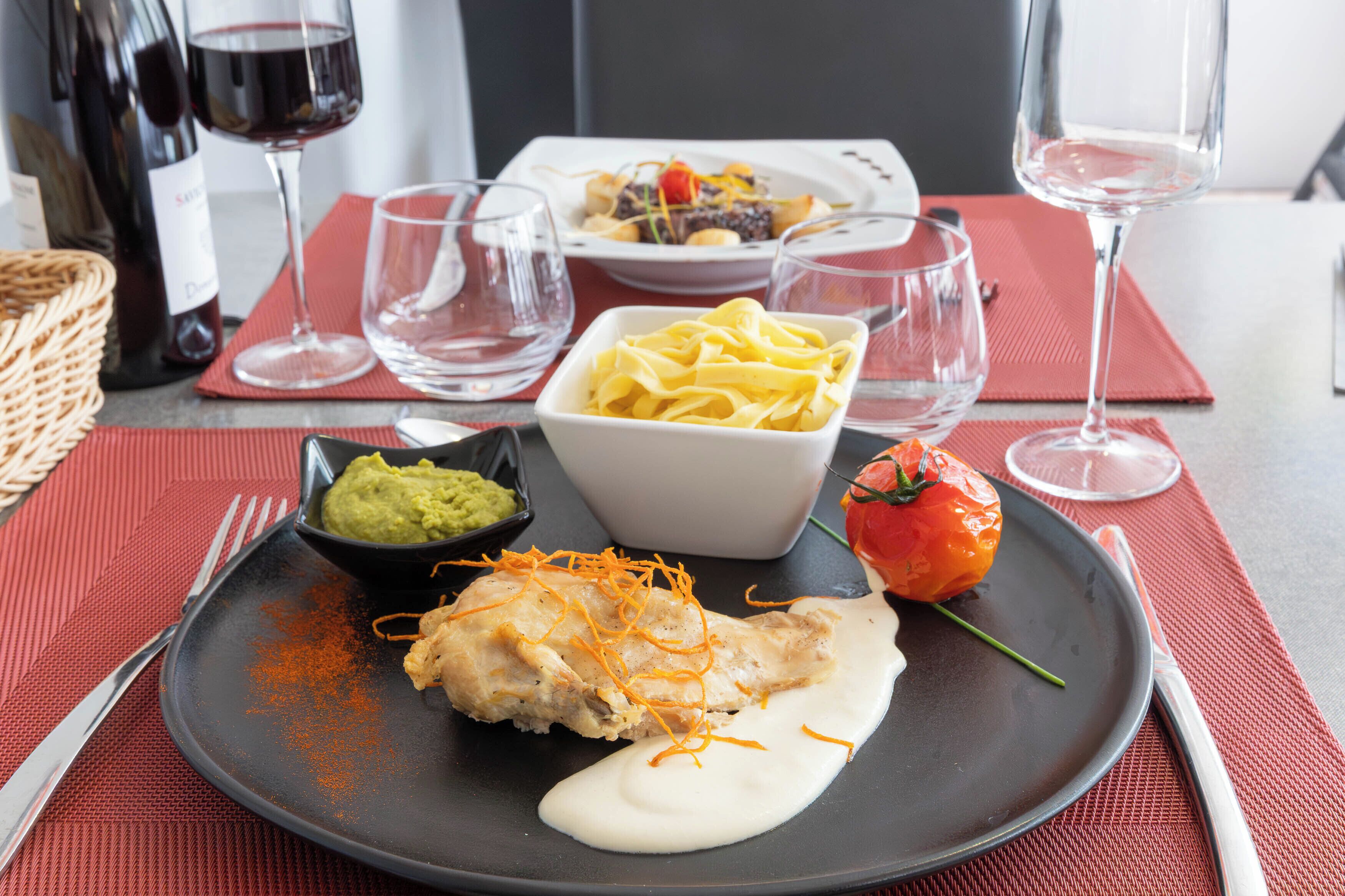 A dining table with plates of food, wine glasses, and a bottle of wine.