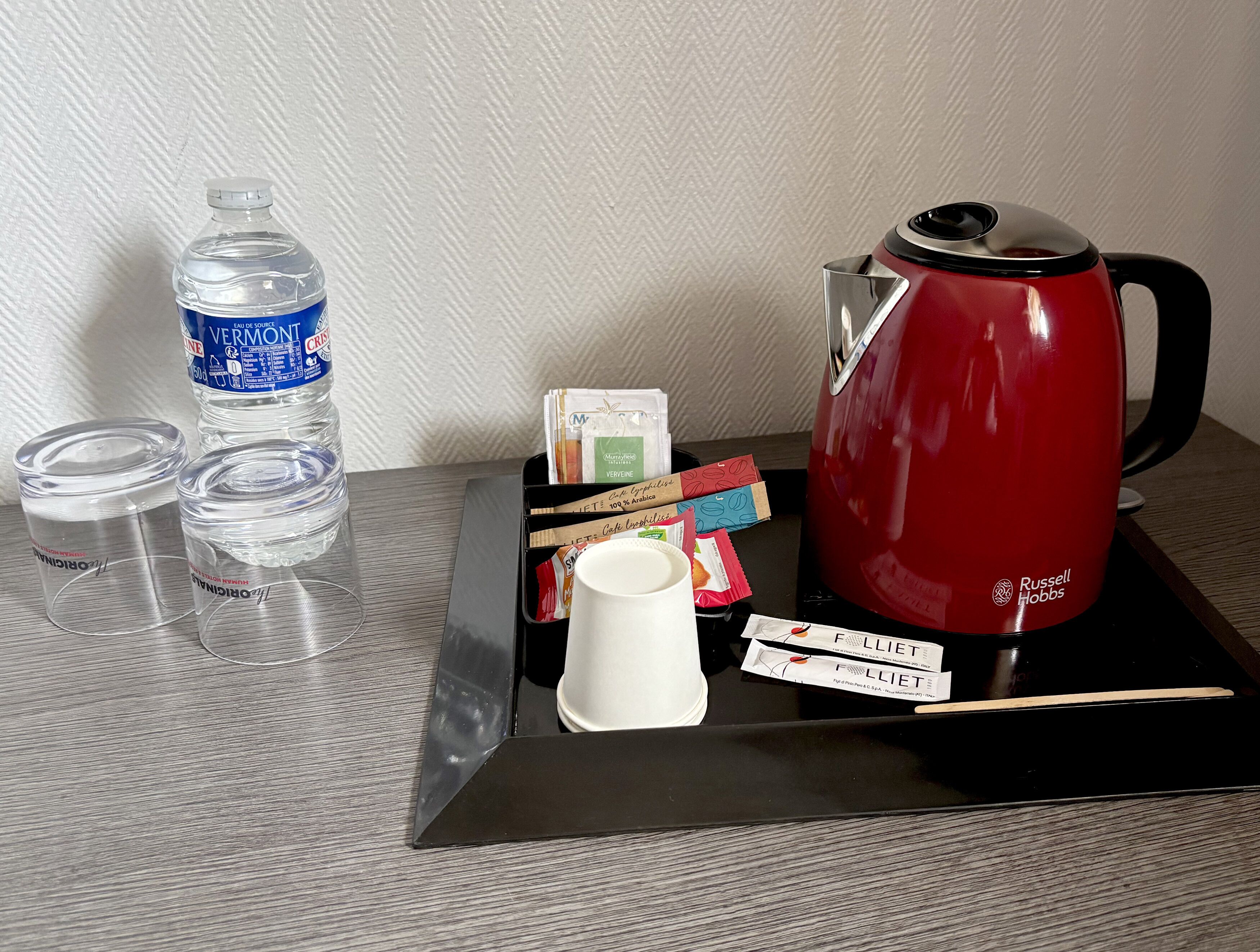 A coffee maker, a bottle of water, and a tray with coffee pods and a cup on a table.