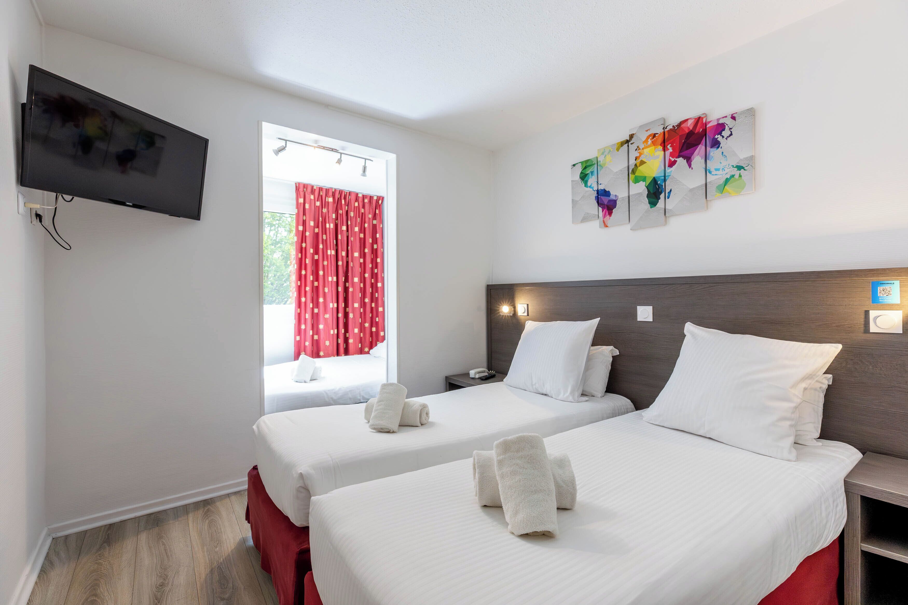 Habitación de hotel con dos camas, un televisor, un ventanal con cortinas rojas y un cuadro de un mapa mundial en la pared.