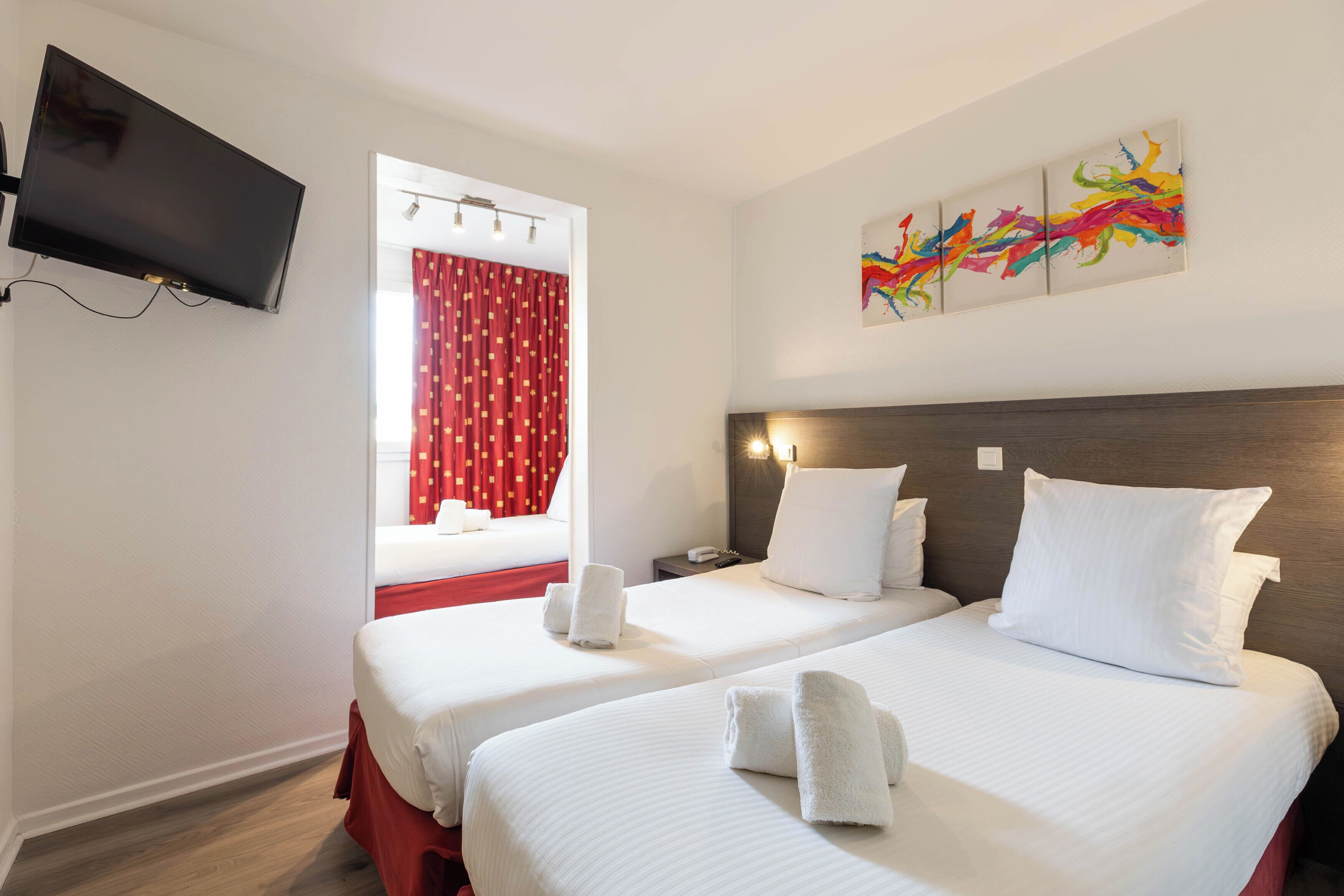 A hotel room with two beds, a TV mounted on the wall, a window with red curtains, and a colorful abstract painting on the wall.