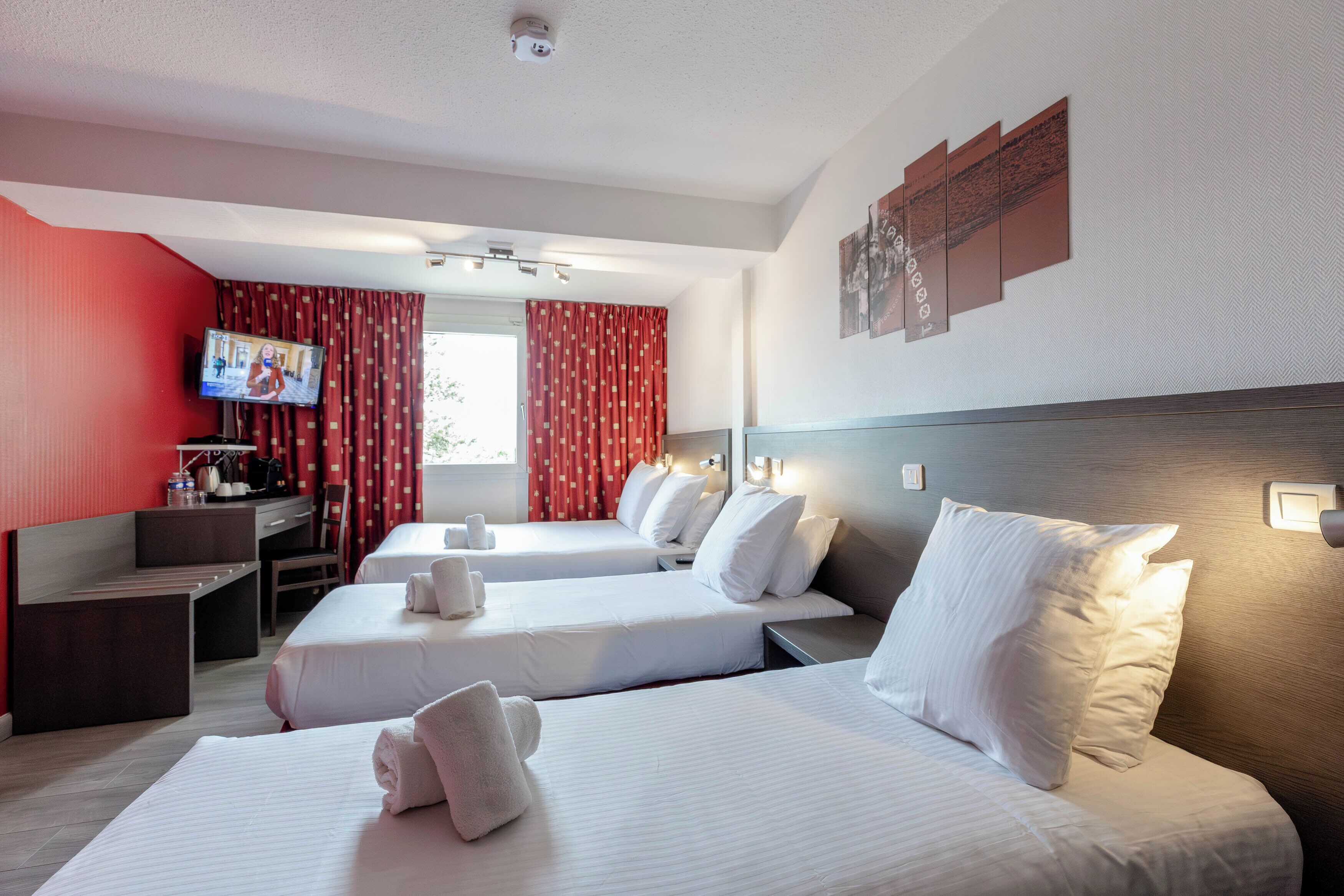 Habitación de hotel con dos camas, un escritorio, un televisor y cortinas rojas.