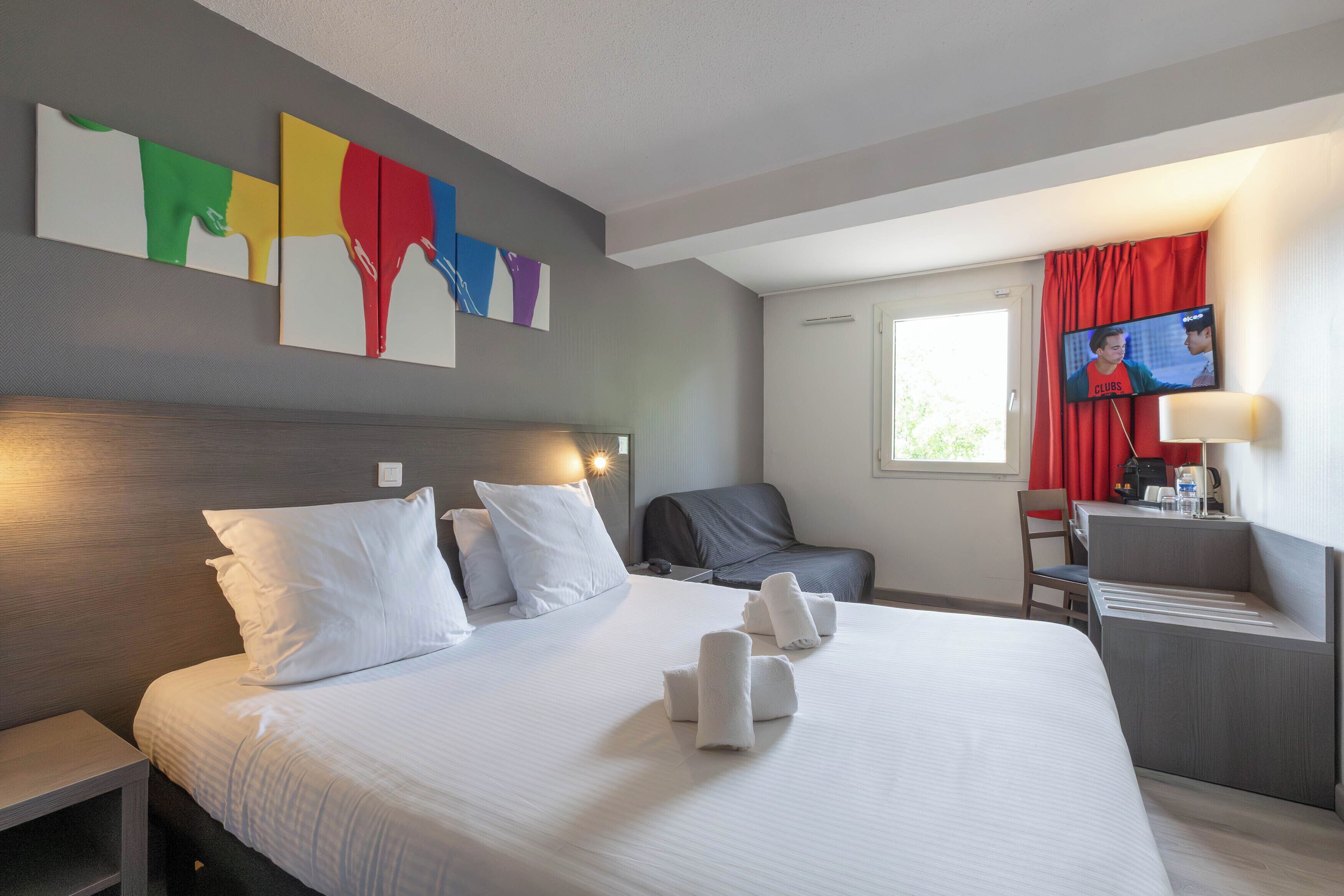 Una habitación de hotel con cama, almohadas, un escritorio con silla, televisión y obras de arte en la pared.