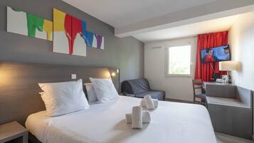 Una habitación de hotel con cama, almohadas, un escritorio con silla, televisión y obras de arte en la pared.
