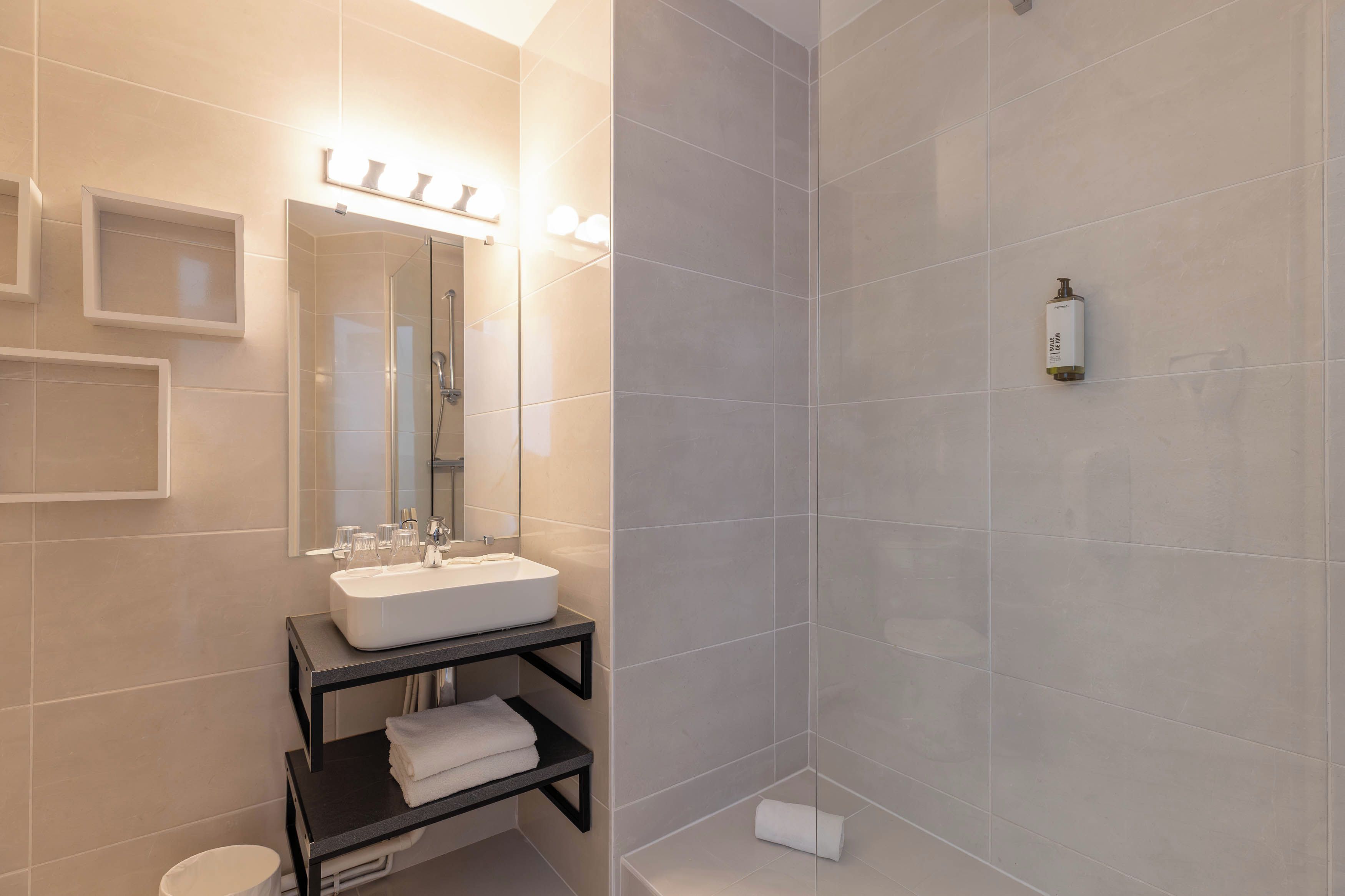 A modern bathroom with a white sink, a glass shower enclosure, and a towel rack.