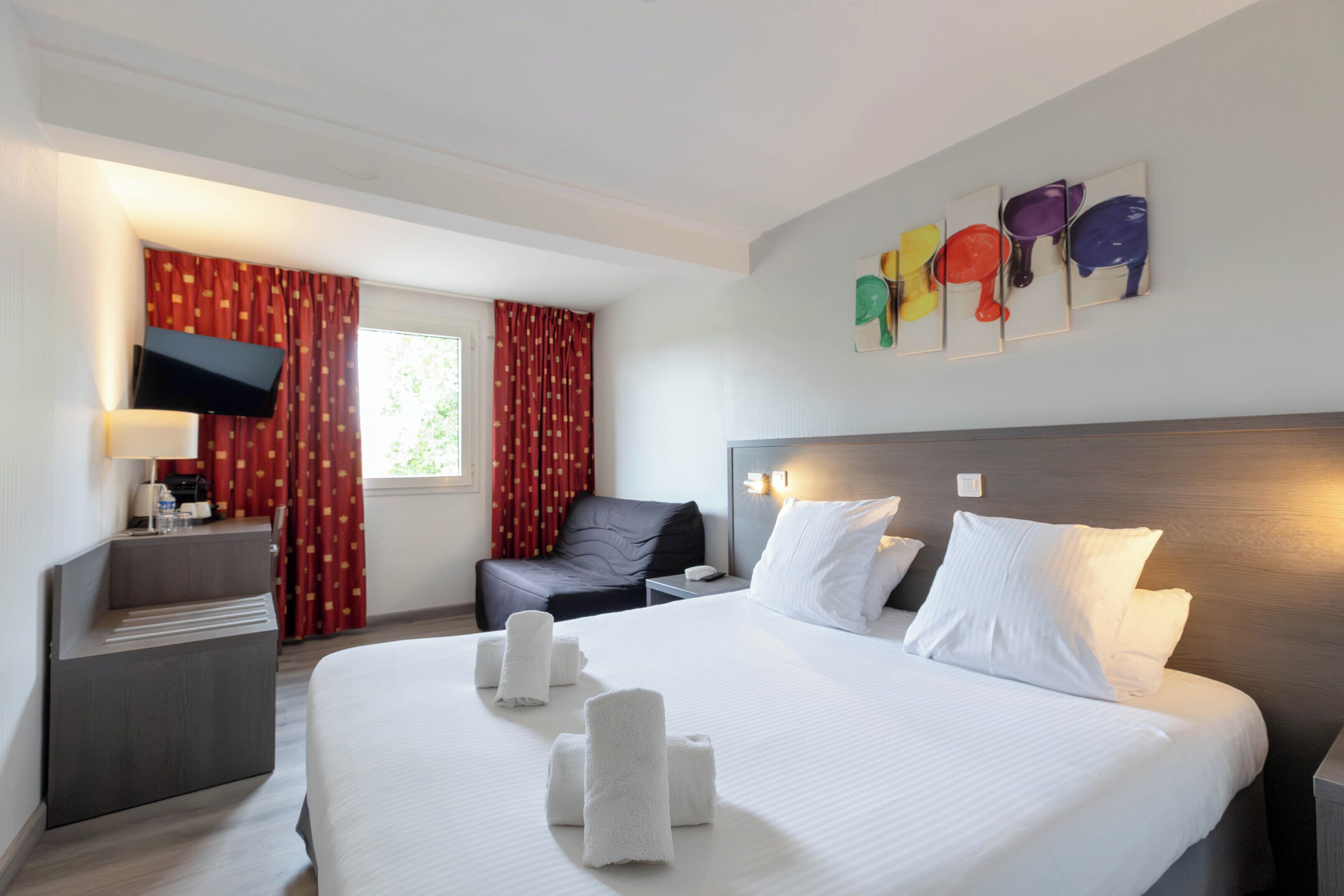 Habitación de hotel con cama, escritorio, silla, televisión y cuadros en la pared.