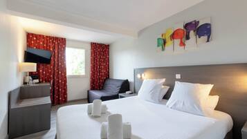 Habitación de hotel con cama, escritorio, silla, televisión y cuadros en la pared.