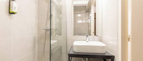 A modern bathroom with a glass shower enclosure, a white sink, and a black countertop.