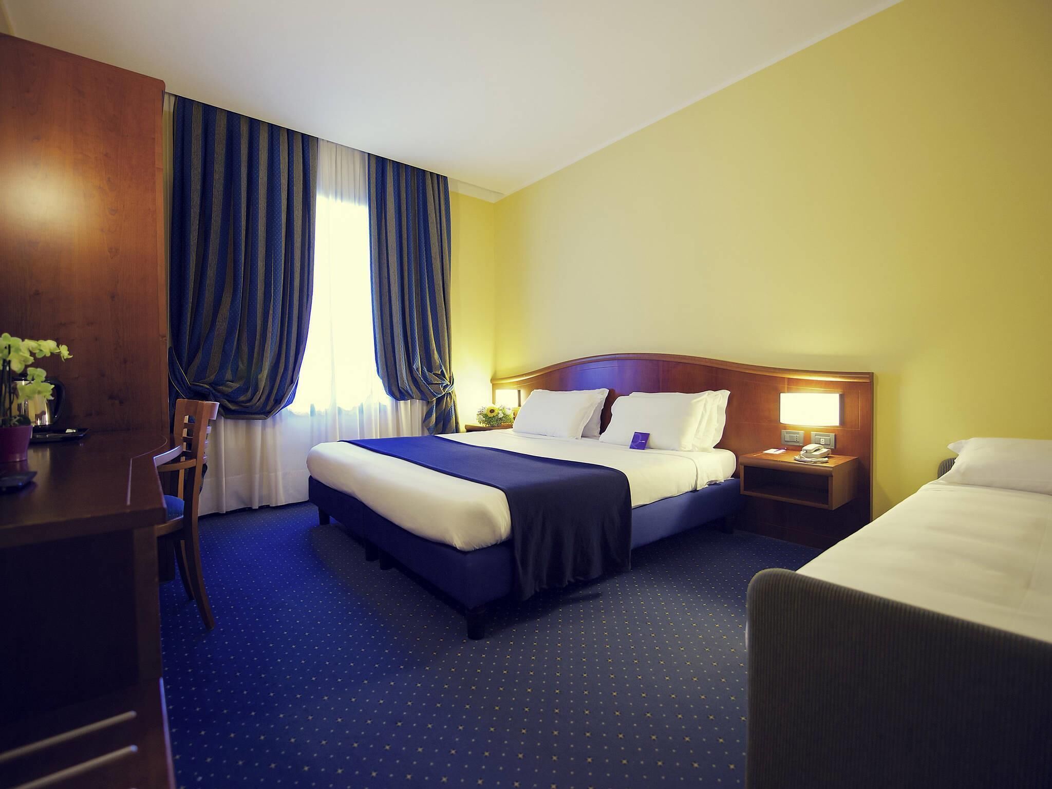 Ein Hotelzimmer mit Bett, Schreibtisch, Stuhl, Nachttisch und einem Fenster mit Vorhängen.