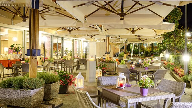 An outdoor dining area with wicker furniture, umbrellas, and potted plants. - Mercure Genova San Biagio (Genoa)