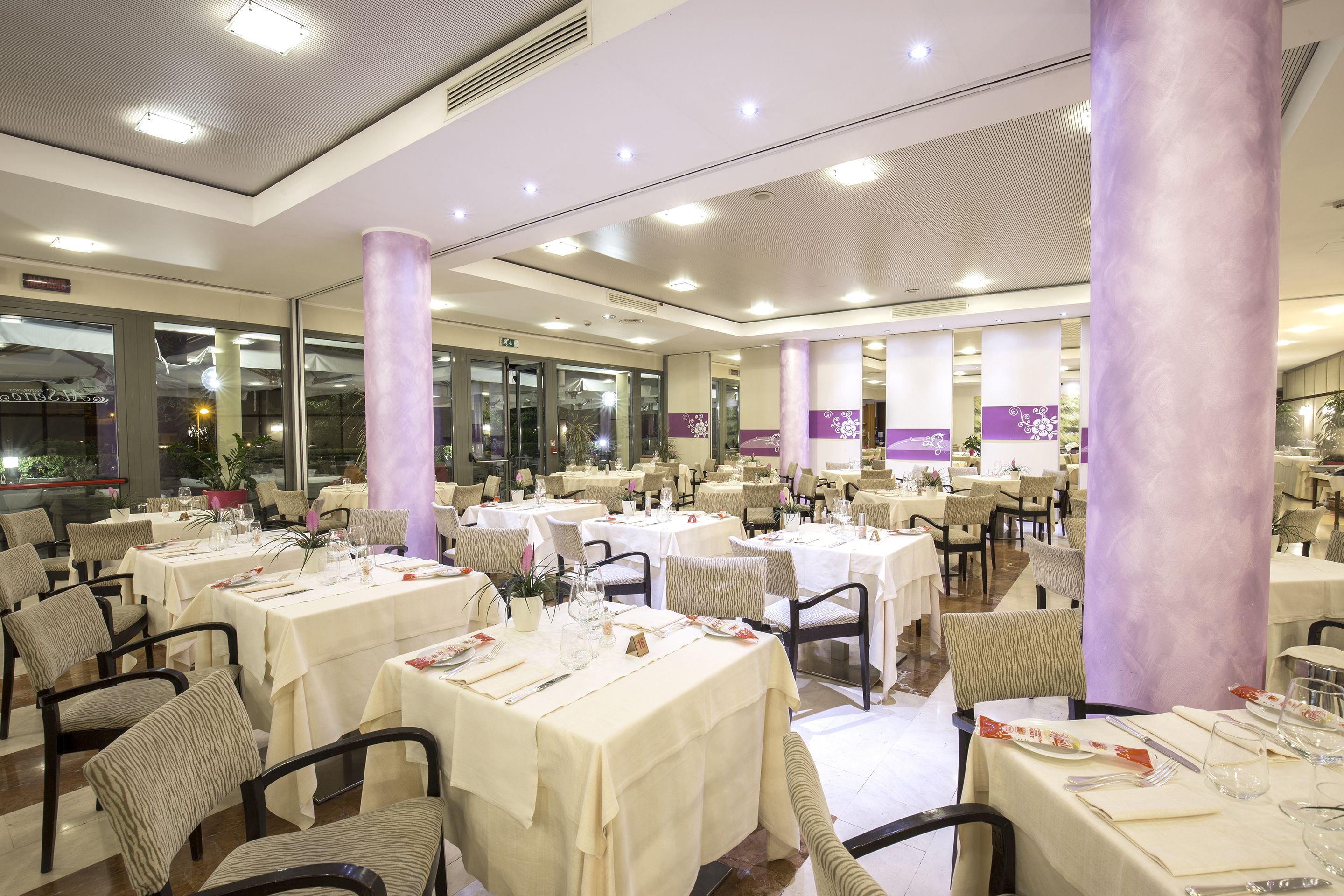 Un restaurante espacioso con numerosas mesas y sillas, ventanas amplias y un diseño de techo moderno.