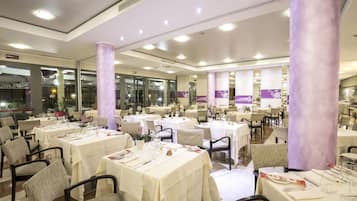 Un restaurante espacioso con numerosas mesas y sillas, ventanas amplias y un diseño de techo moderno.