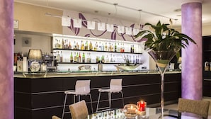 A bar area with a glass table, chairs, a martini glass, and a shelf of liquor bottles. - Mercure Genova San Biagio (Genoa)