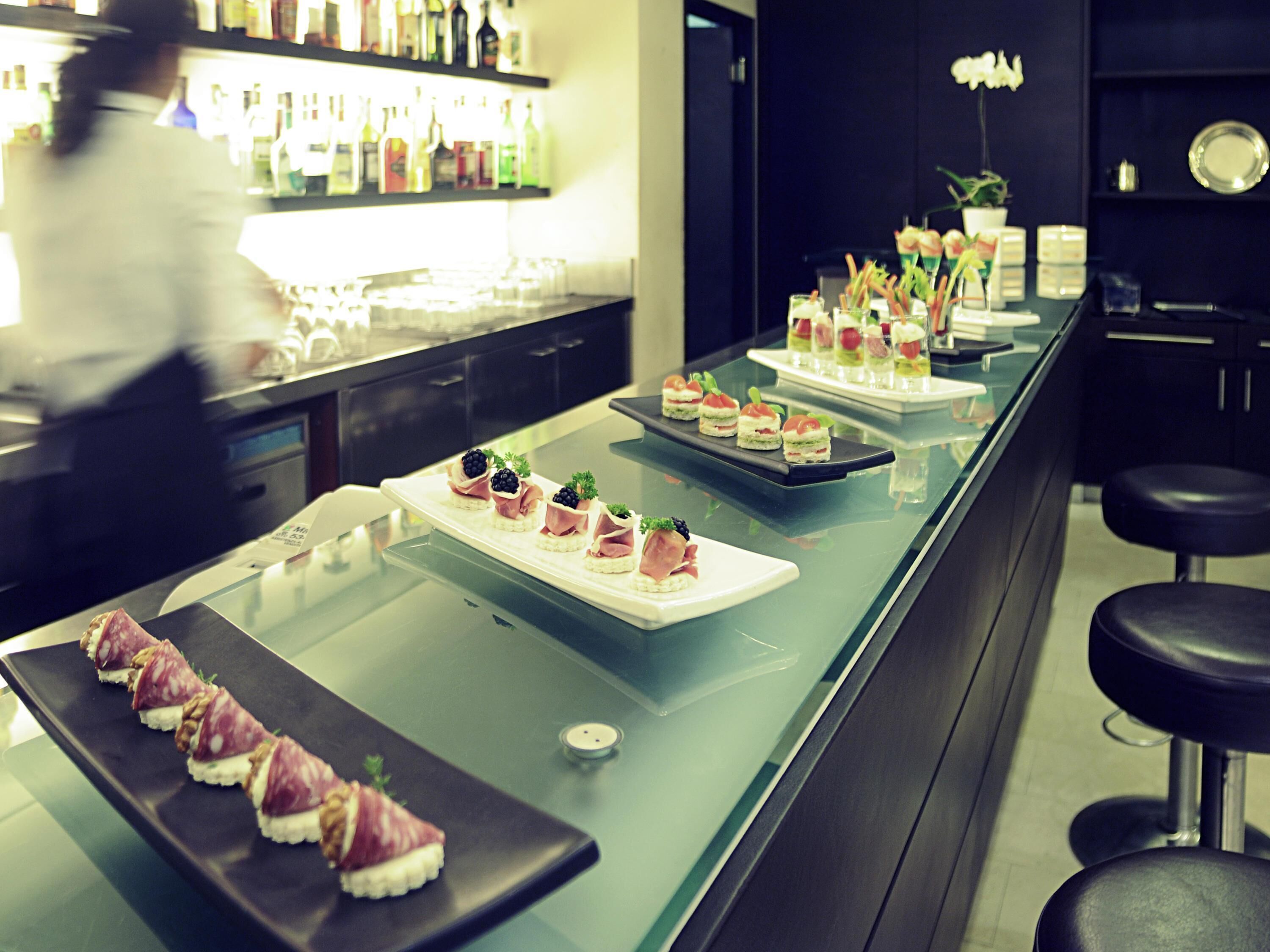 A bar area with neatly arranged appetizers on trays, a bar counter, and a seating area with stools.
