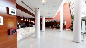 A spacious lobby with a reception desk, large white columns, and a modern ceiling design. - Mercure Genova San Biagio (Genoa)